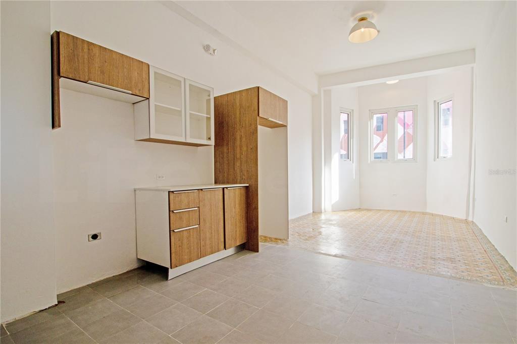 A kitchen area with wood-toned cabinets and gray tile flooring opens into a sunlit room — 319 RECINTO SUR STREET UNIT 2, SAN JUAN, PR