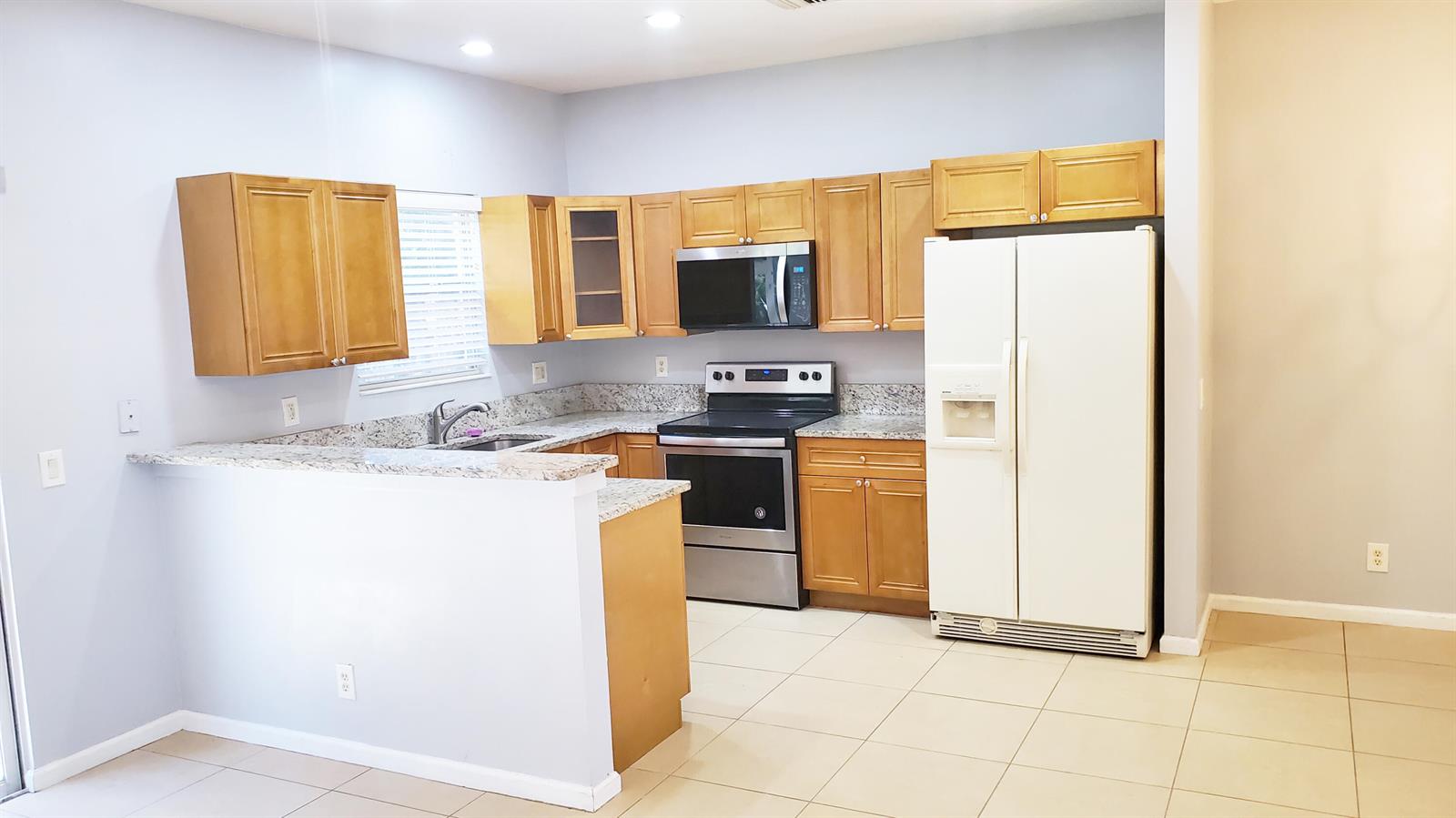 A kitchen with light wood cabinets, granite countertops, stainless steel appliances, and a white refrigerator — 132 Baldwin Boulevard, FL 33463, FL