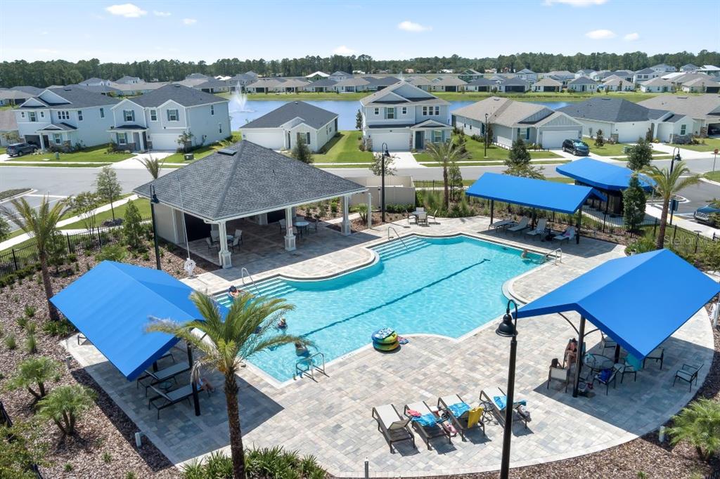 An aerial view shows a community swimming pool with blue shade structures and lounge chairs — 104 WAVERLY, PALM COAST, FL