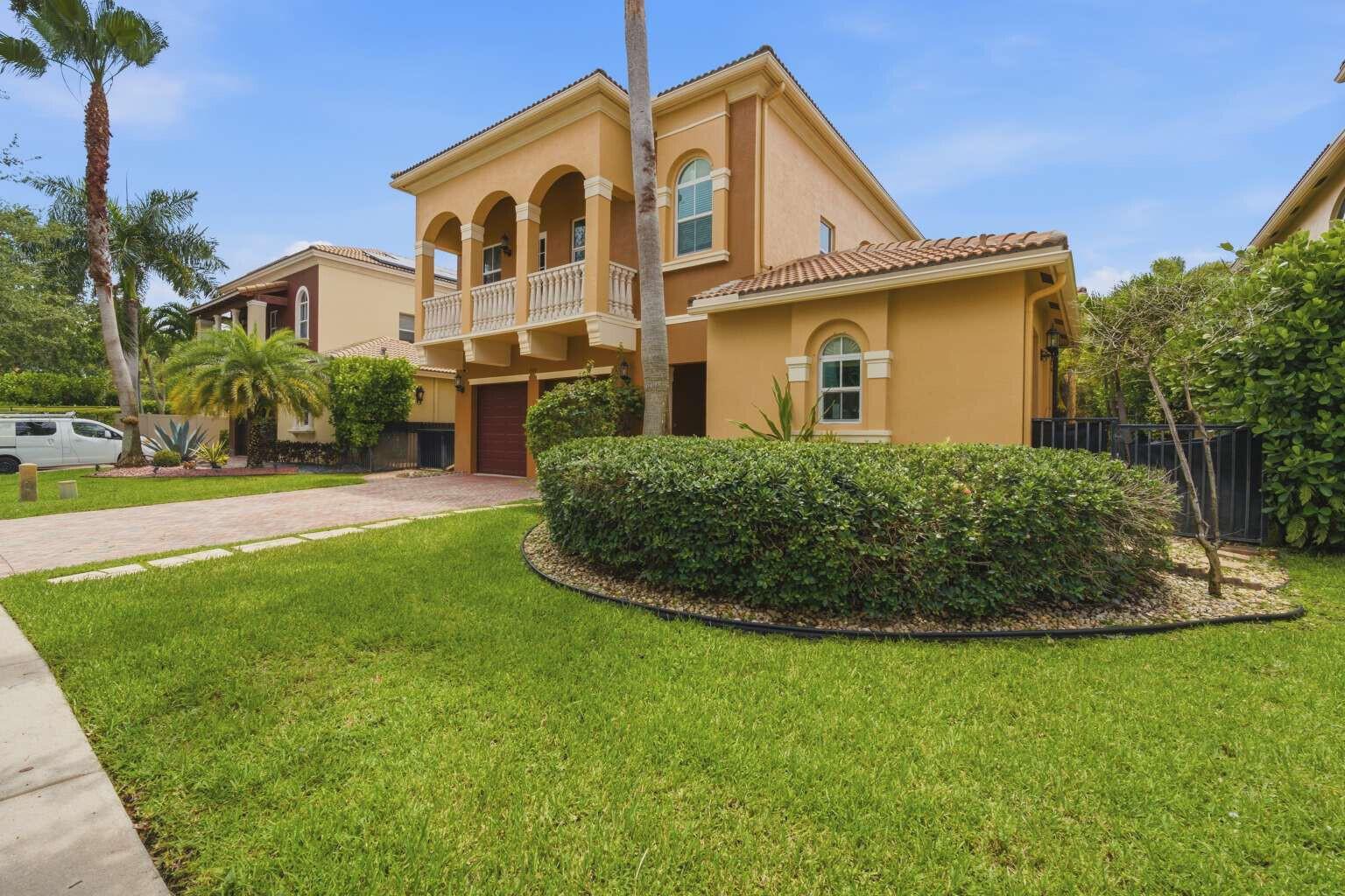 A two-story yellow stucco house features a second-floor balcony, arched windows, and a manicured hedge — 9190 Nugent Trail, West Palm Beach FL 33411, WEST PALM BEACH, FL