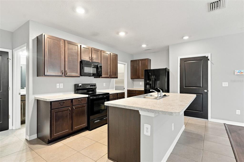 A kitchen with dark wood cabinets, black appliances, a central island, and light-colored countertops — 6647 SEAWAY DRIVE, BROOKSVILLE, FL
