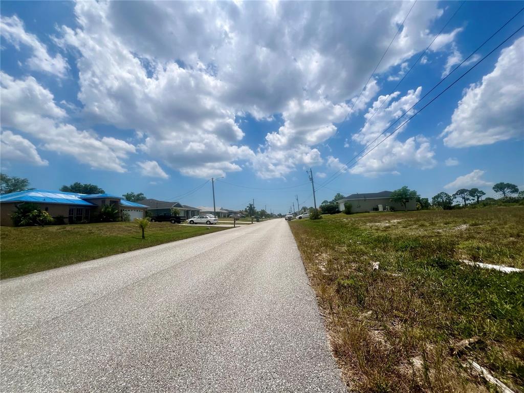 A paved residential street stretches between a grassy vacant lot and several single-story houses — 1623 NW 26TH STREET, CAPE CORAL, FL