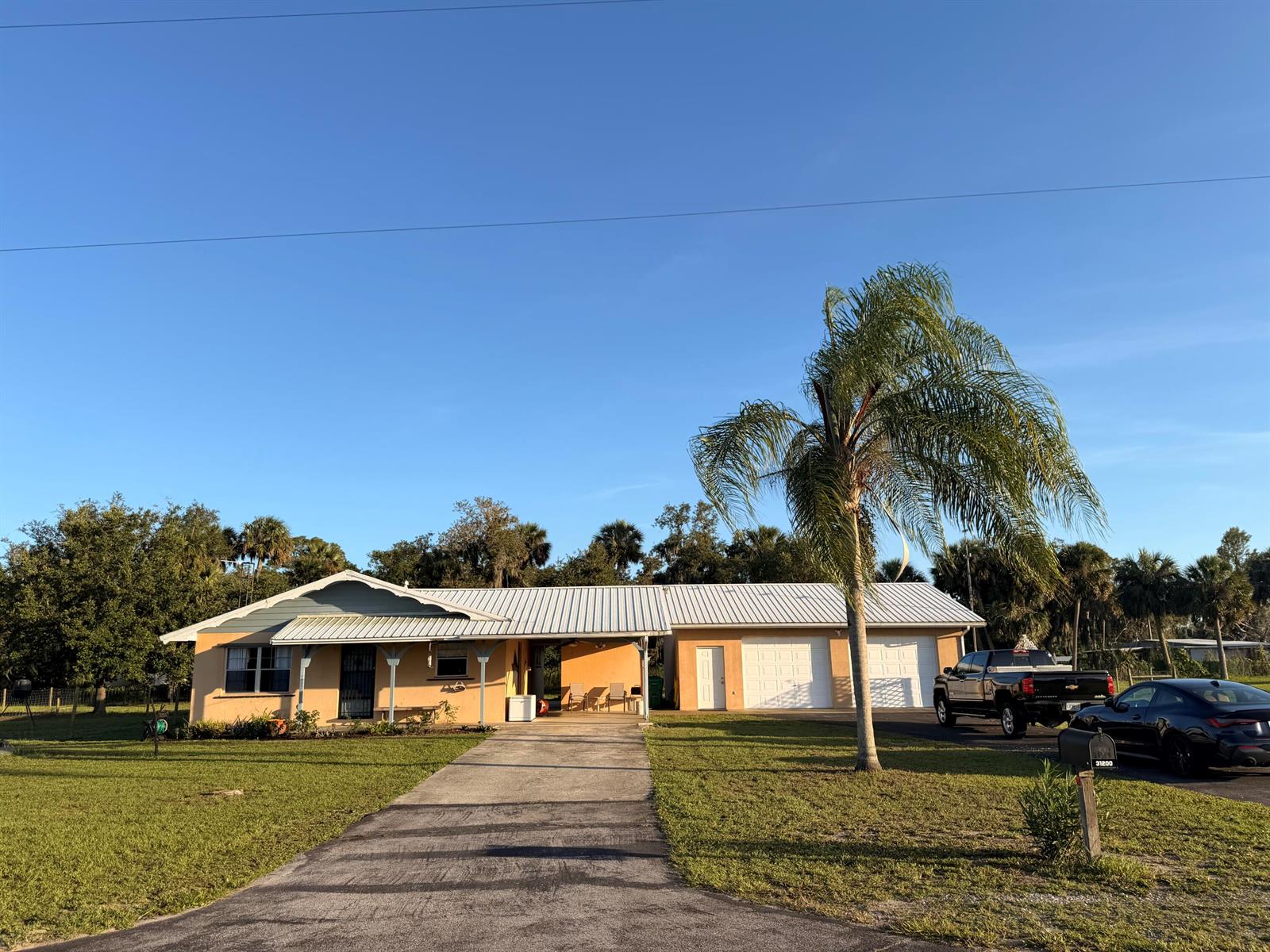 A single-story house with a metal roof, attached garage, and a palm tree in front — 31200 Us-441, Okeechobee FL 34972, OKEECHOBEE, FL
