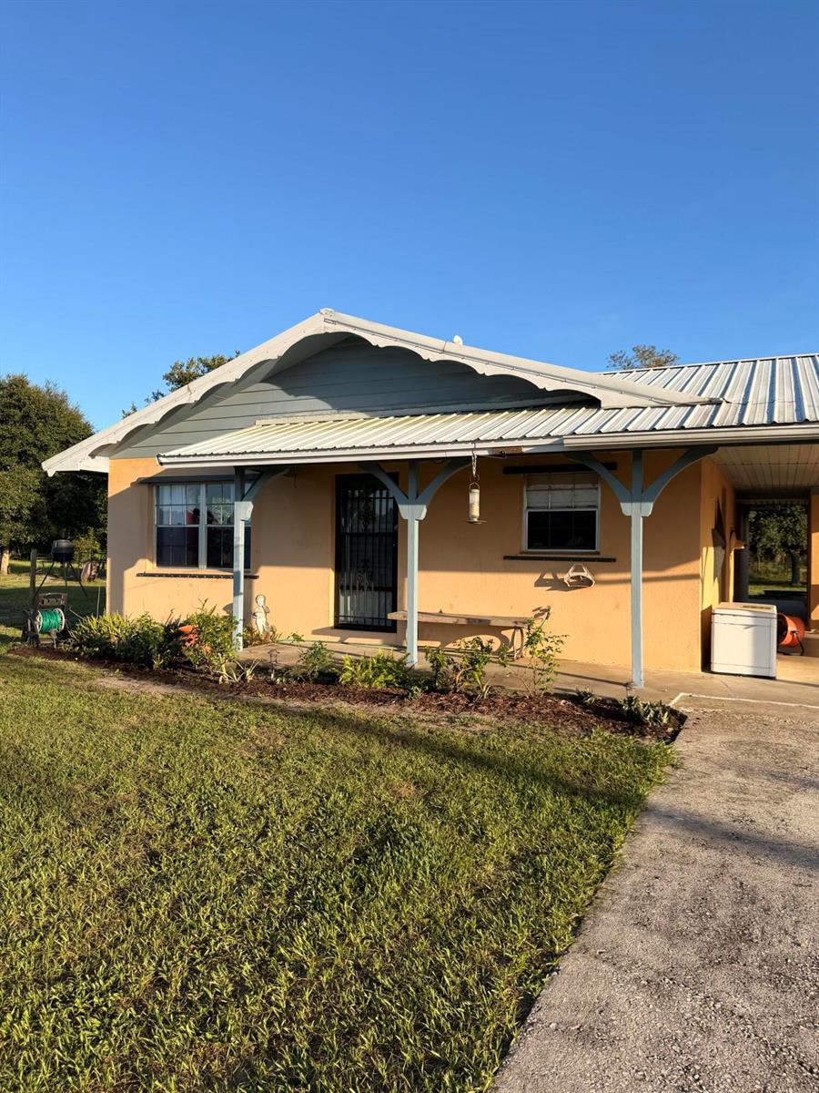 A single-story peach-colored house features a metal roof, a front porch, and a concrete driveway — 31200 Us-441, Okeechobee FL 34972, OKEECHOBEE, FL