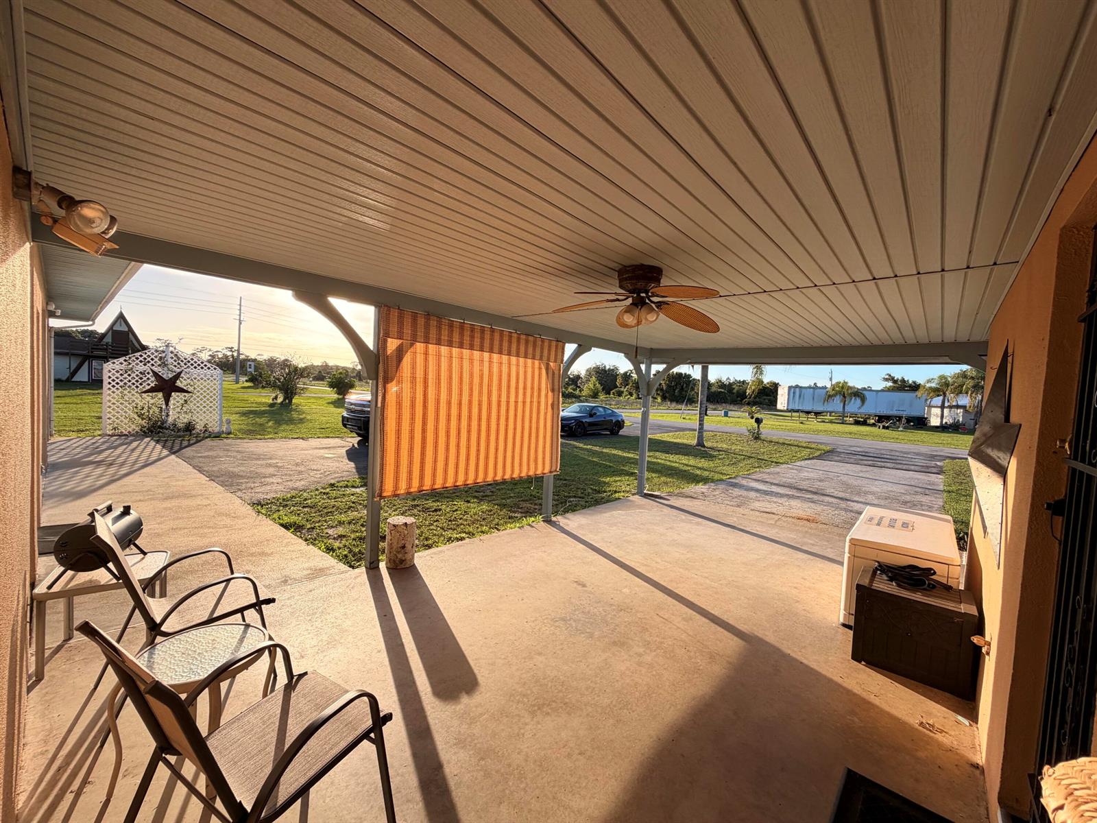 A covered concrete patio features a ceiling fan, outdoor seating, and a striped privacy shade — 31200 Us-441, Okeechobee FL 34972, OKEECHOBEE, FL