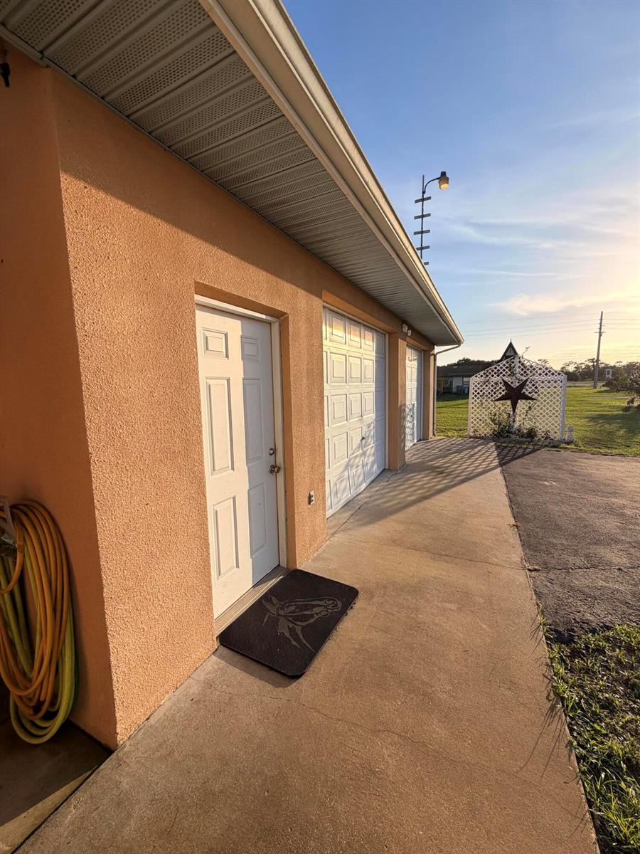 An exterior view of a peach-colored garage with a side door and concrete walkway — 31200 Us-441, Okeechobee FL 34972, OKEECHOBEE, FL