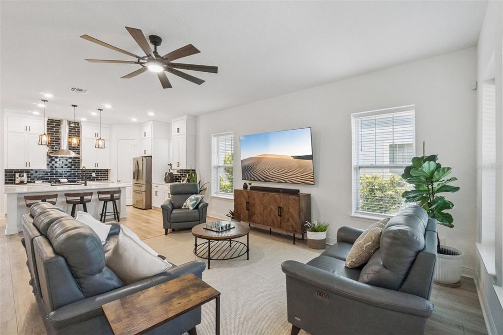 A living room with gray leather furniture, a large television, and an open-concept kitchen — 6839 BRIDGMAN STREET, ORLANDO, FL