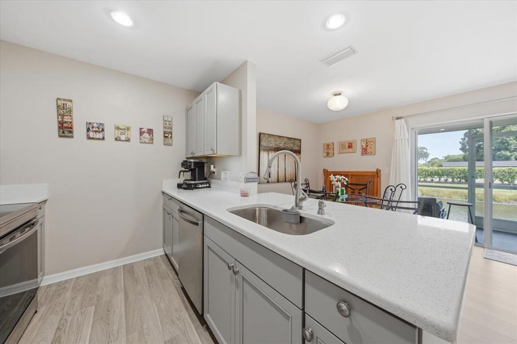 A kitchen with grey cabinets, white countertops, and a stainless steel sink overlooks a dining area — 5503 67TH UNIT 18, PINELLAS PARK, FL