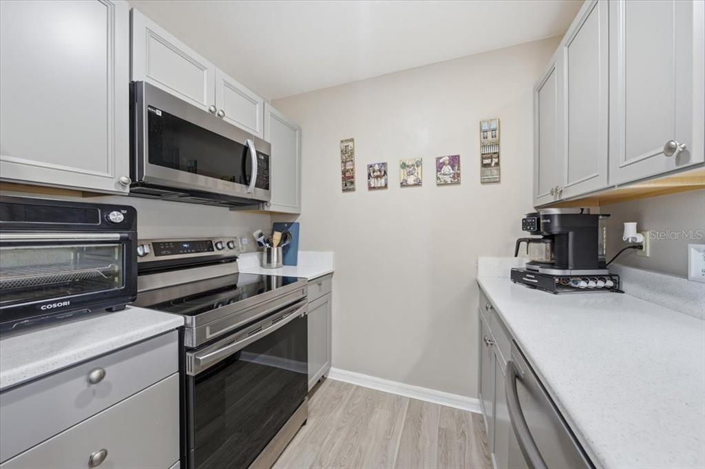 A galley-style kitchen features grey cabinets, stainless steel appliances, and light-colored countertops — 5503 67TH UNIT 18, PINELLAS PARK, FL
