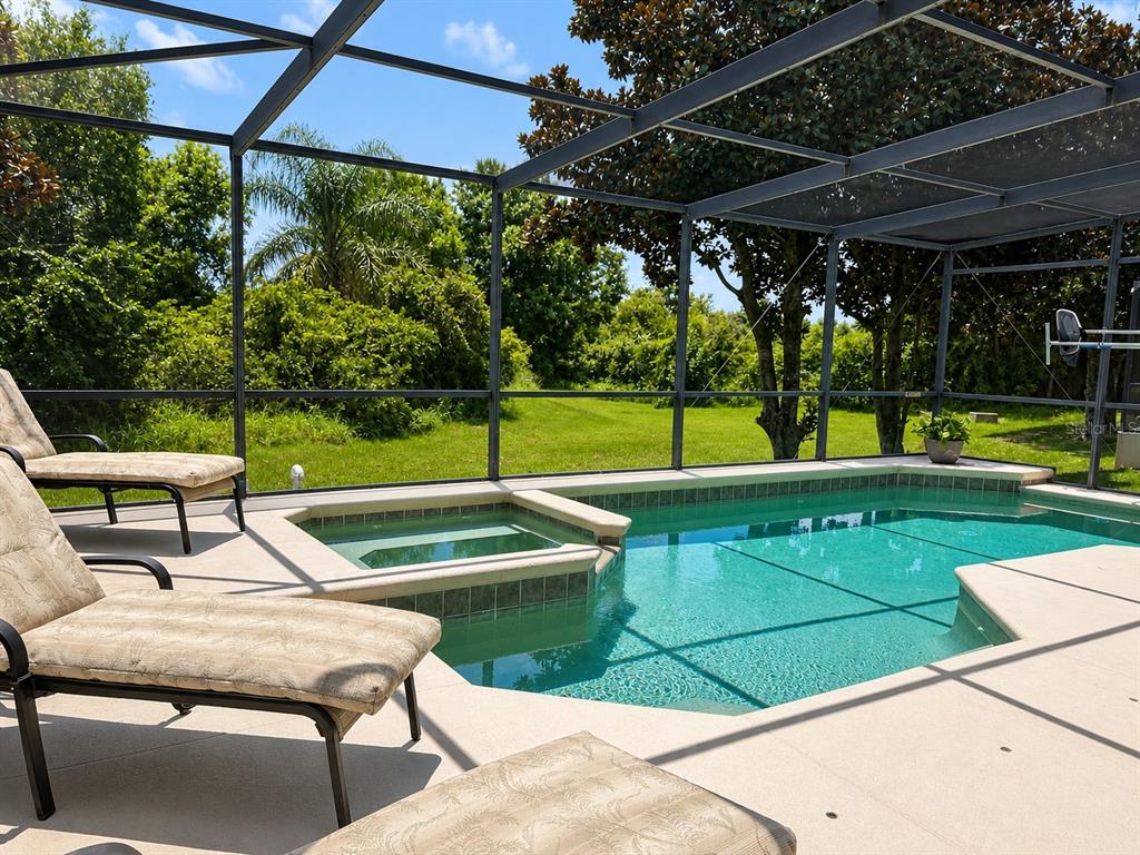A screened-in pool and spa area with lounge chairs overlooking a grassy backyard — 880 SUFFOLK PLACE, DAVENPORT, FL