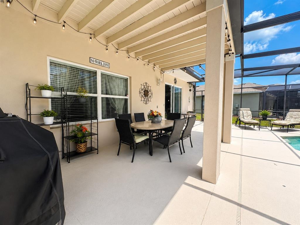 A covered patio features a dining set, a metal shelving unit, and a pool view — 880 SUFFOLK PLACE, DAVENPORT, FL