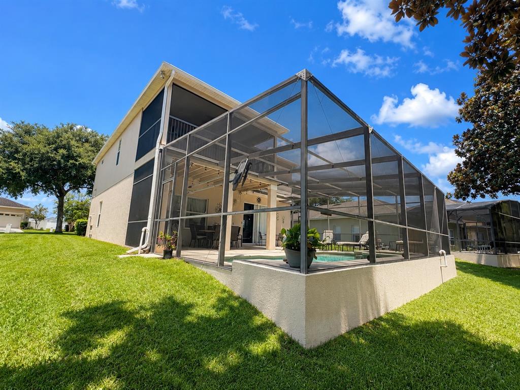 A two-story house features a screened-in pool enclosure and a grassy backyard under a blue sky — 880 SUFFOLK PLACE, DAVENPORT, FL