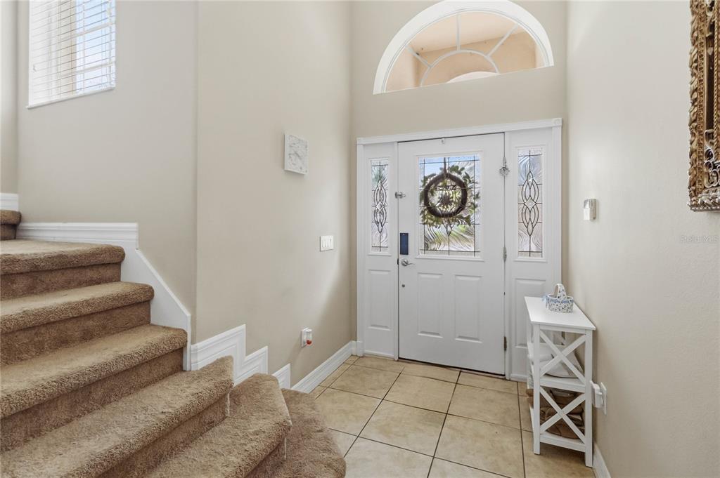 An entryway features a carpeted staircase, tile flooring, a white front door, and a transom window — 880 SUFFOLK PLACE, DAVENPORT, FL