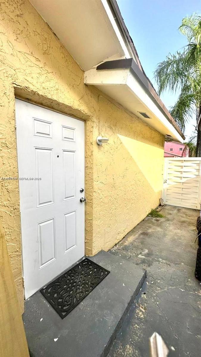 A white exterior door with a black mat sits on a concrete patio — 233 NE 199th Ter # 0, Miami FL 33179, MIAMI, FL
