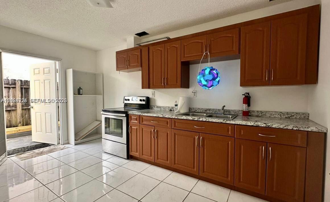 A kitchen features wood cabinets, granite countertops, stainless steel appliances, and white tile flooring — 233 NE 199th Ter # 0, Miami FL 33179, MIAMI, FL
