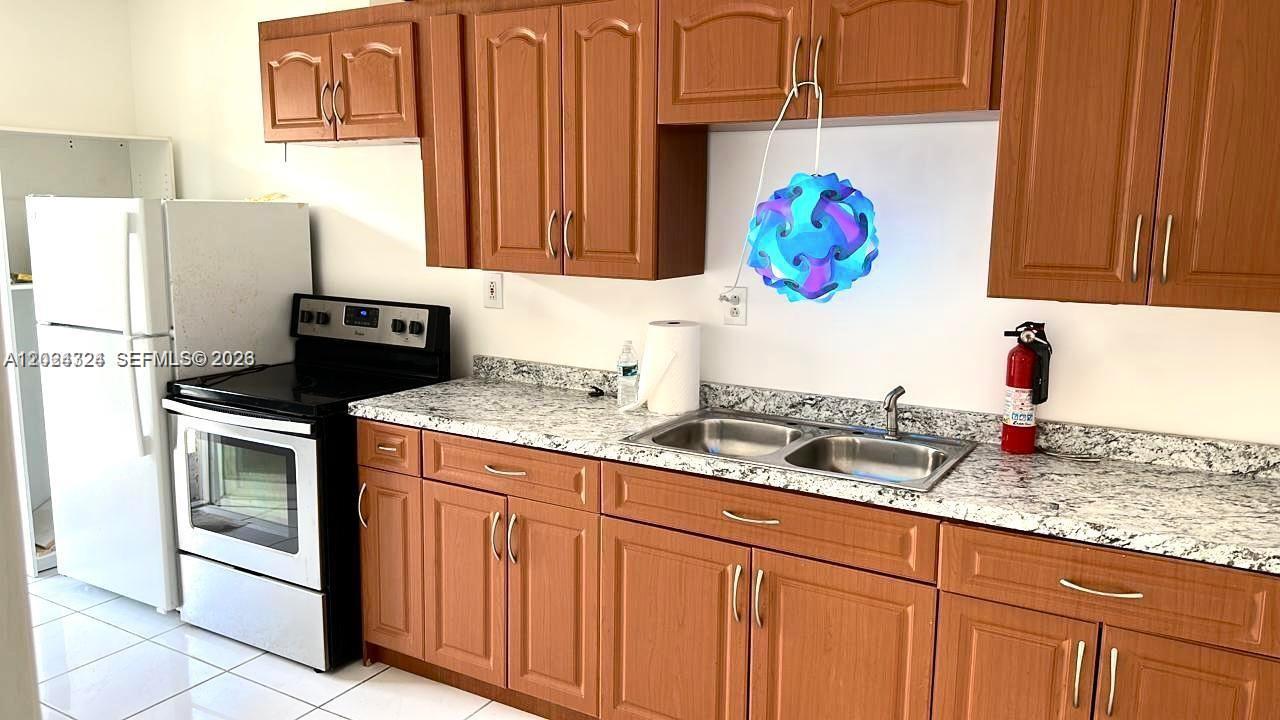 A kitchen features wood cabinets, granite countertops, a double sink, and a white stove — 233 NE 199th Ter # 0, Miami FL 33179, MIAMI, FL