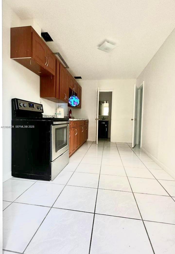 A galley kitchen features wood cabinets, a black stove, and white tile flooring — 233 NE 199th Ter # 0, Miami FL 33179, MIAMI, FL