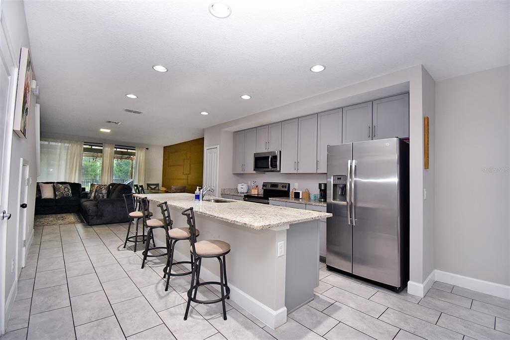 A kitchen with gray cabinets, granite countertops, and a breakfast bar overlooks a living area — 4734 TERRA ESMERALDA, KISSIMMEE, FL