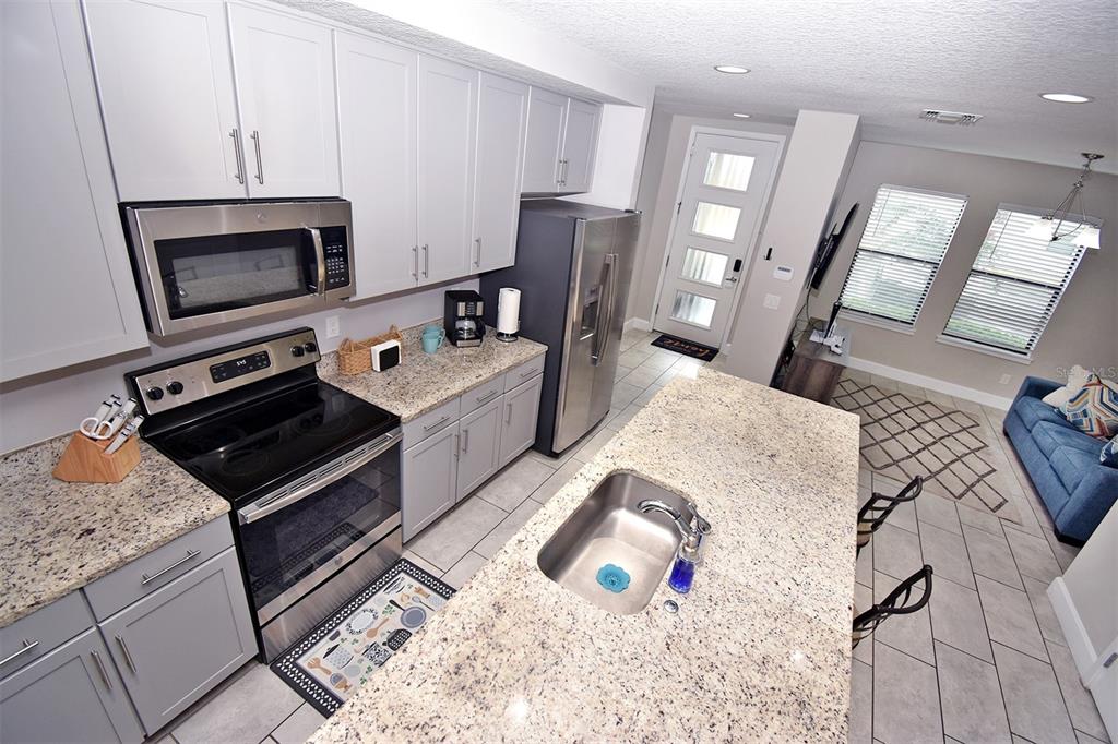 A modern kitchen features gray cabinets, granite countertops, stainless steel appliances, and an island sink — 4734 TERRA ESMERALDA, KISSIMMEE, FL