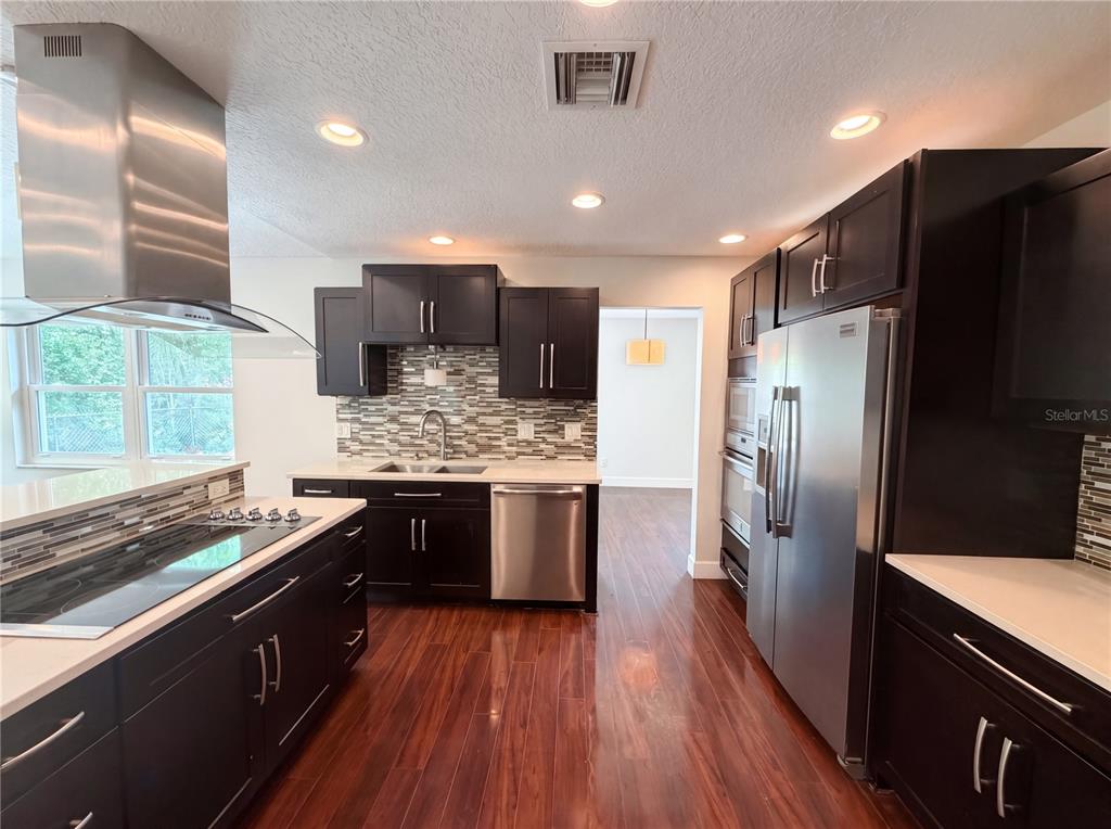 A kitchen features dark wood cabinets, stainless steel appliances, and a mosaic tile backsplash — 13804 CANDIDATE PLACE, TAMPA, FL