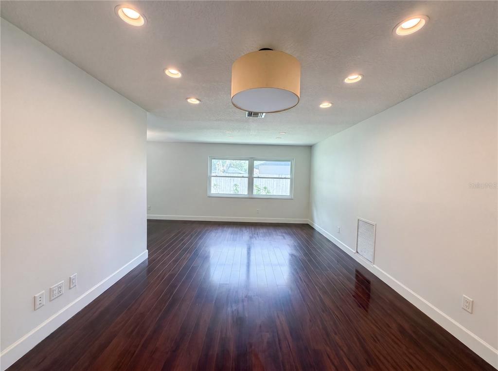 An empty room features dark hardwood floors, white walls, recessed lighting, and a central pendant light — 13804 CANDIDATE PLACE, TAMPA, FL