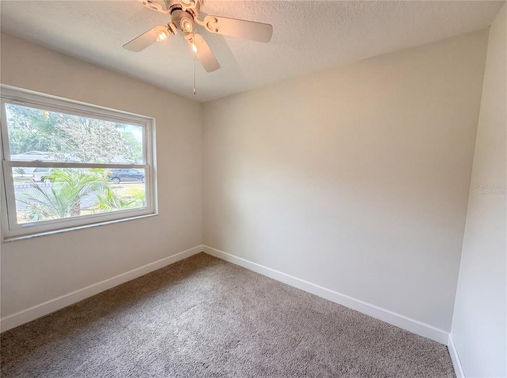 An empty bedroom features beige walls, carpeted flooring, a ceiling fan, and a single window — 13804 CANDIDATE PLACE, TAMPA, FL
