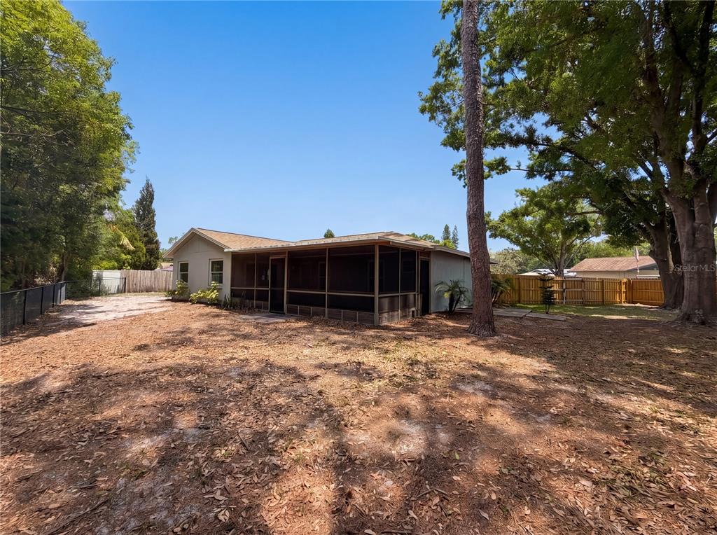A backyard view of a house with a screened-in porch and surrounding trees — 13804 CANDIDATE PLACE, TAMPA, FL