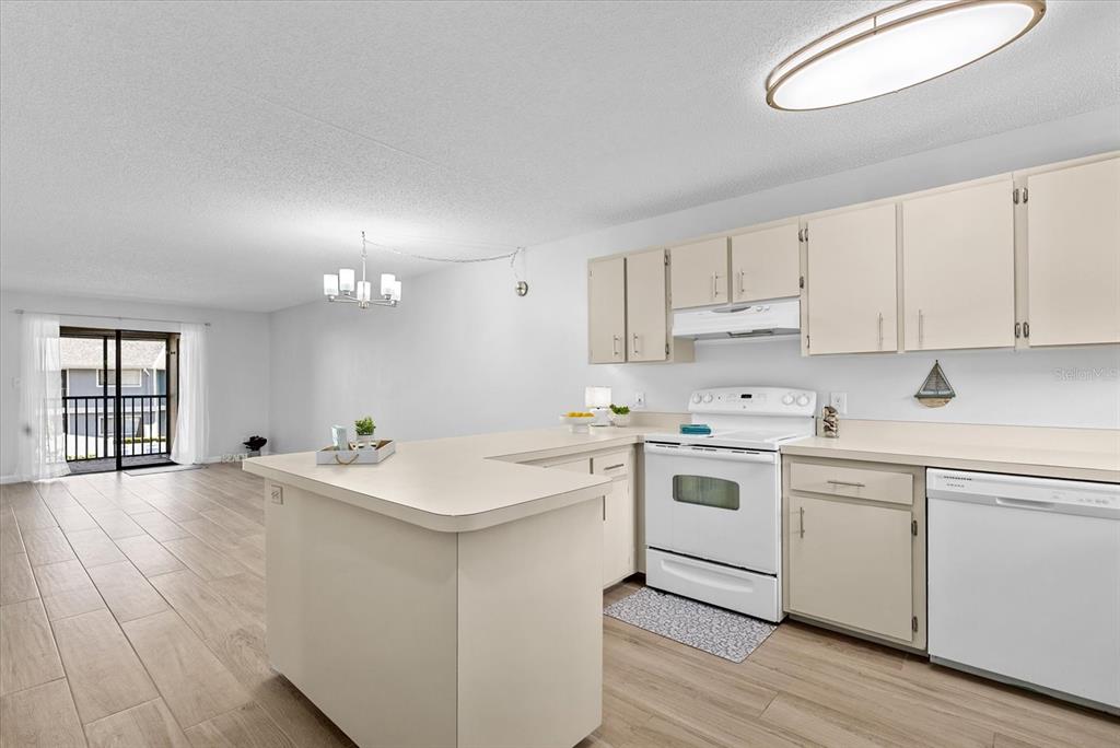 A kitchen with beige cabinets and white appliances opens to a living area with tile flooring — 6033 34TH STREET W UNIT 28, BRADENTON, FL