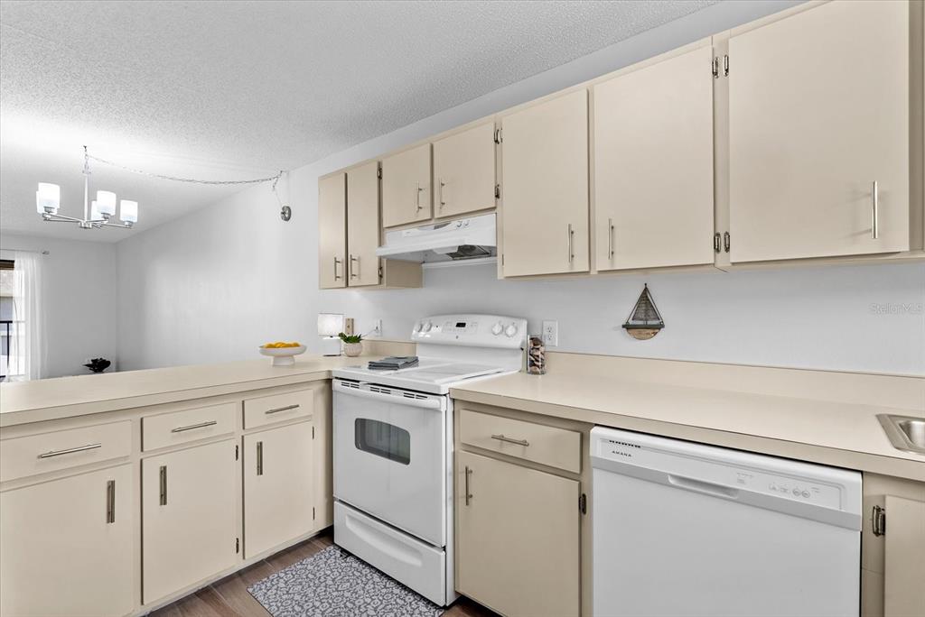A kitchen features beige cabinets, white appliances, and a peninsula counter overlooking a dining area — 6033 34TH STREET W UNIT 28, BRADENTON, FL