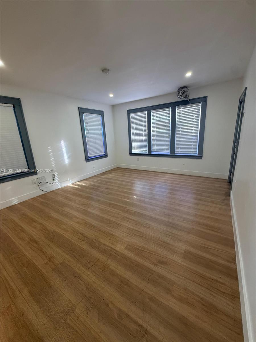 An empty room features light wood-look flooring, white walls, and windows with dark frames — 453 NW 25th Ct # 1, Miami FL 33125, MIAMI, FL