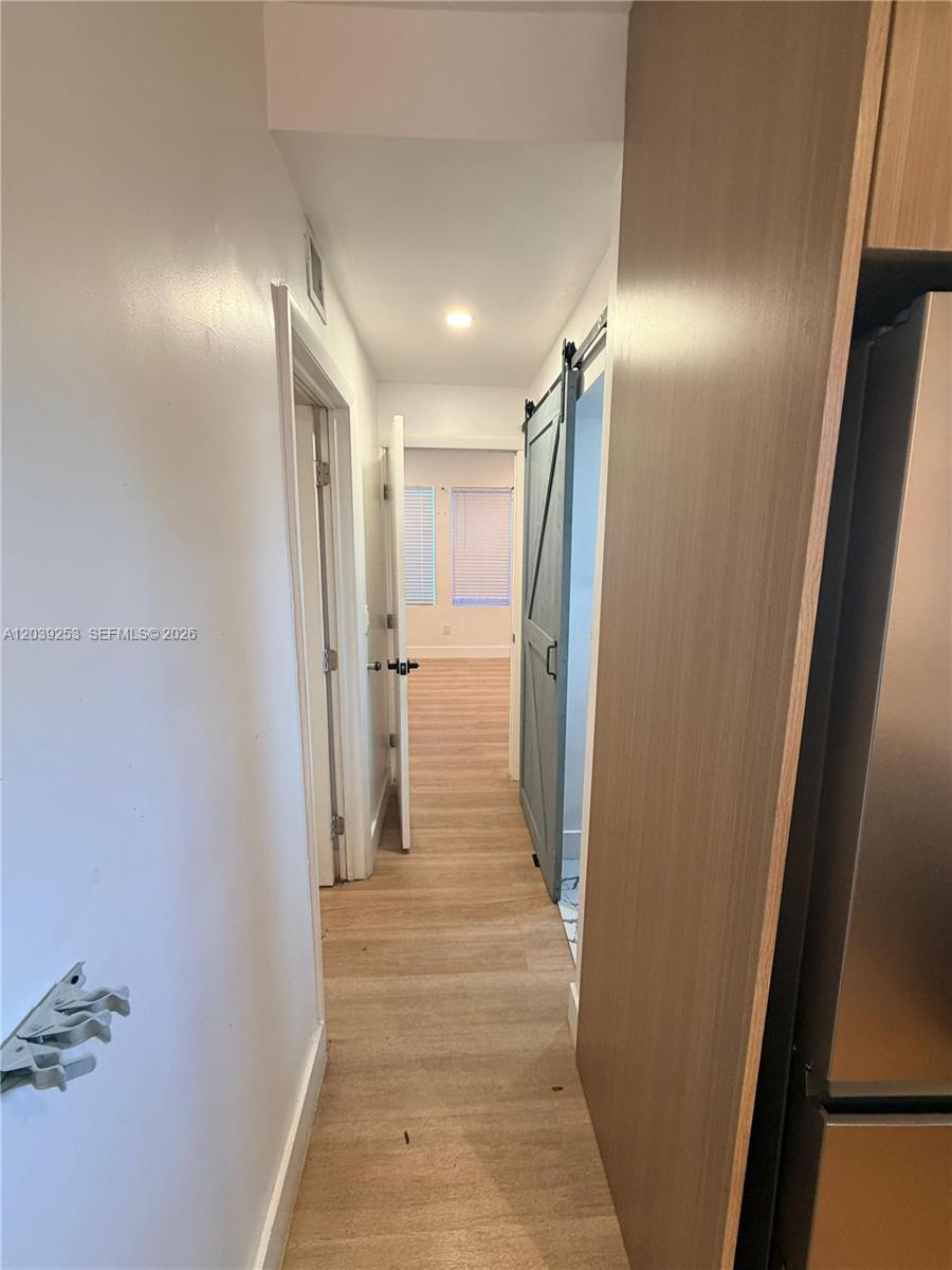 A hallway with light wood flooring leads to a bedroom featuring a blue sliding door — 453 NW 25th Ct # 1, Miami FL 33125, MIAMI, FL