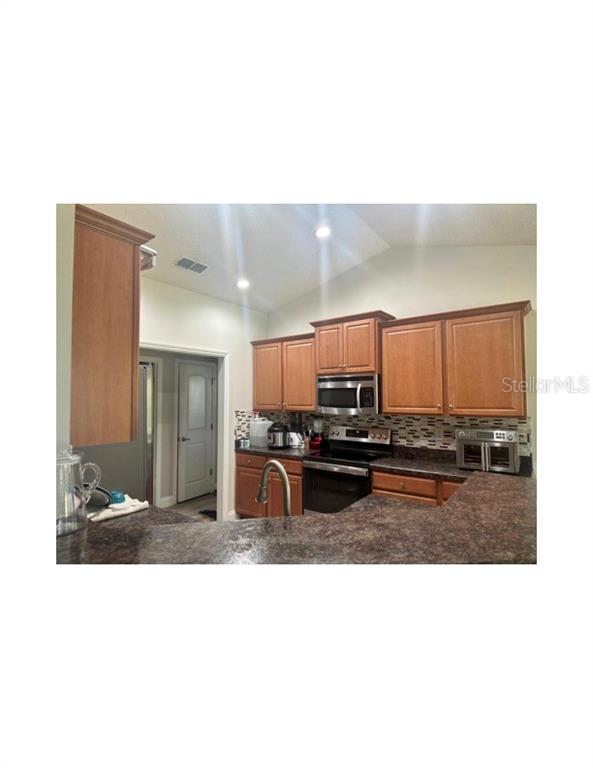 A kitchen features wood cabinets, dark countertops, stainless steel appliances, and a tiled backsplash — 41 PRIMROSE, PALM COAST, FL