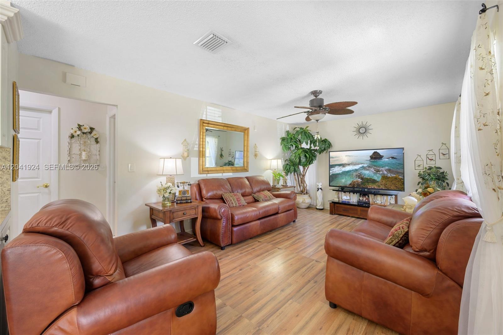 A living room features brown leather furniture, wood-look flooring, and a television on a stand — 906 SW 8th Ave, Hallandale Beach FL 33009, HALLANDALE BEACH, FL