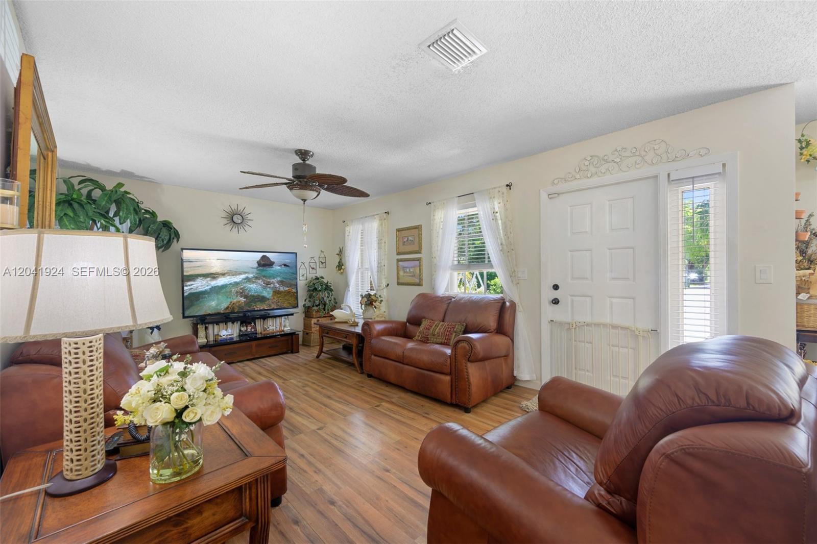 A living room features brown leather furniture, wood-look flooring, and a ceiling fan — 906 SW 8th Ave, Hallandale Beach FL 33009, HALLANDALE BEACH, FL