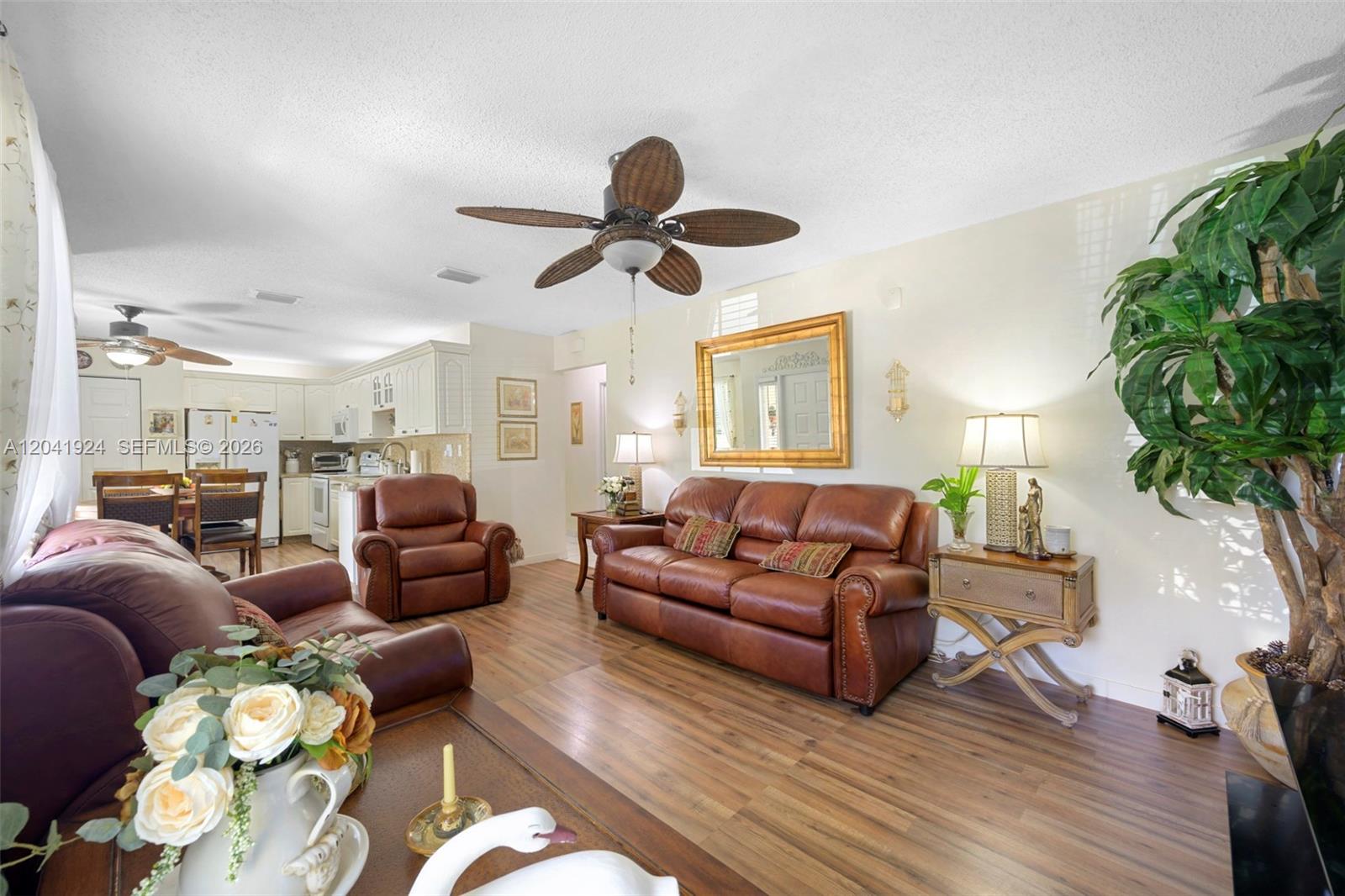A living room features leather furniture, wood-look flooring, a ceiling fan, and an open kitchen — 906 SW 8th Ave, Hallandale Beach FL 33009, HALLANDALE BEACH, FL