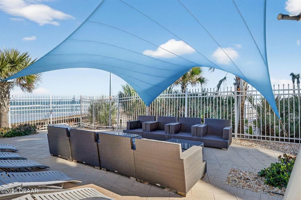 An outdoor patio features a blue shade sail, wicker lounge furniture, and a metal fence — 3703 S ATLANTIC AVENUE UNIT 504, DAYTONA BEACH SHORES, FL