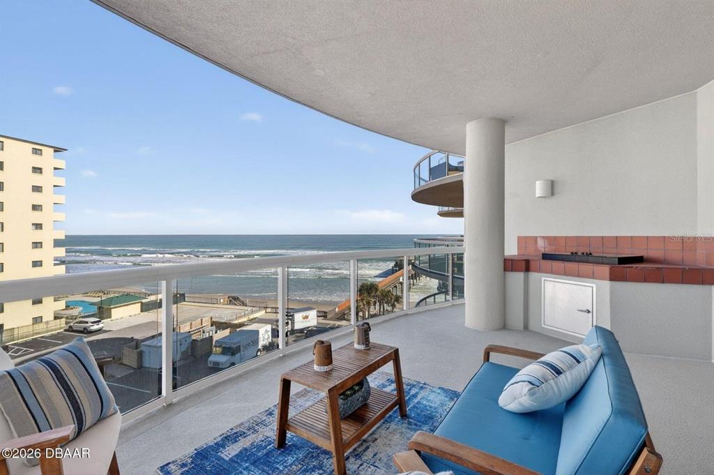 A balcony with a built-in grill overlooks the ocean and a neighboring high-rise building — 3703 S ATLANTIC AVENUE UNIT 504, DAYTONA BEACH SHORES, FL