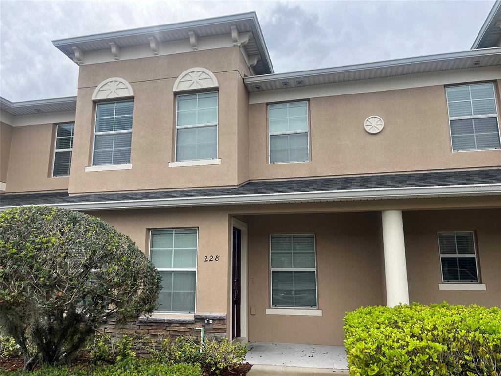 A two-story townhouse exterior features tan stucco walls, a covered entryway, and arched windows — 228 CARINA CIRCLE, SANFORD, FL