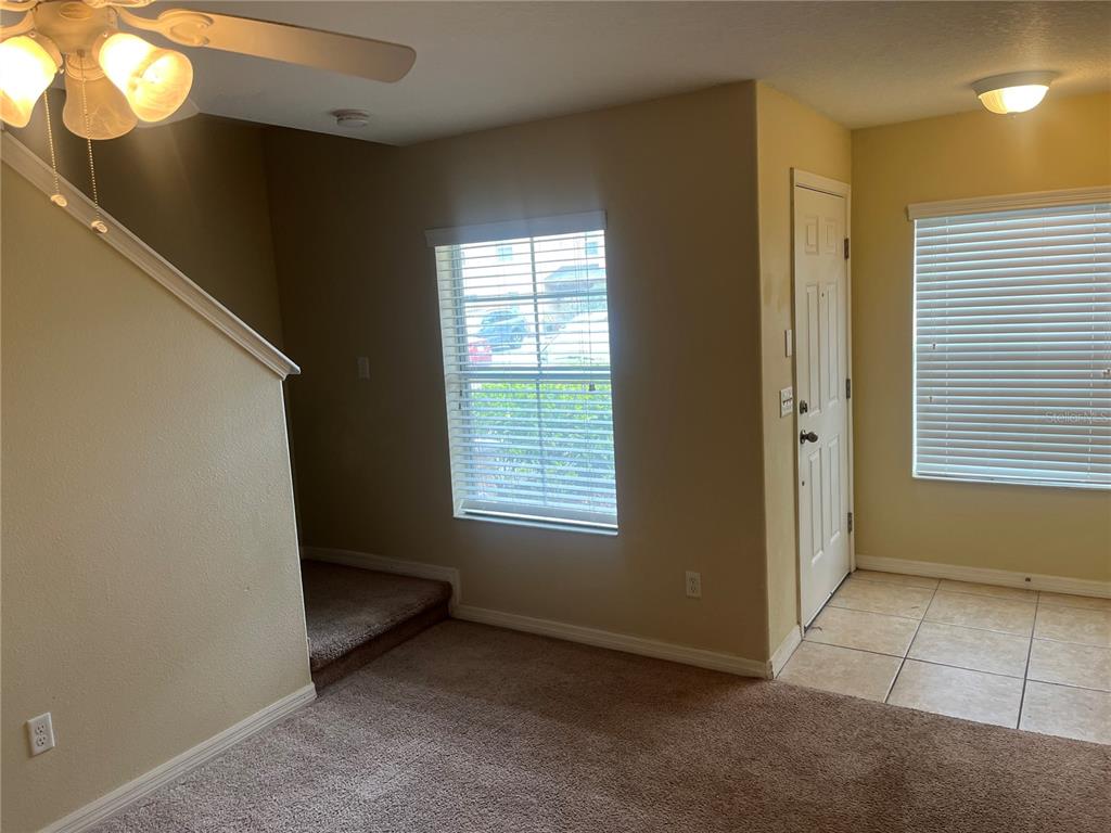 A living area with carpeted flooring, a ceiling fan, a window, and a tiled entryway — 228 CARINA CIRCLE, SANFORD, FL