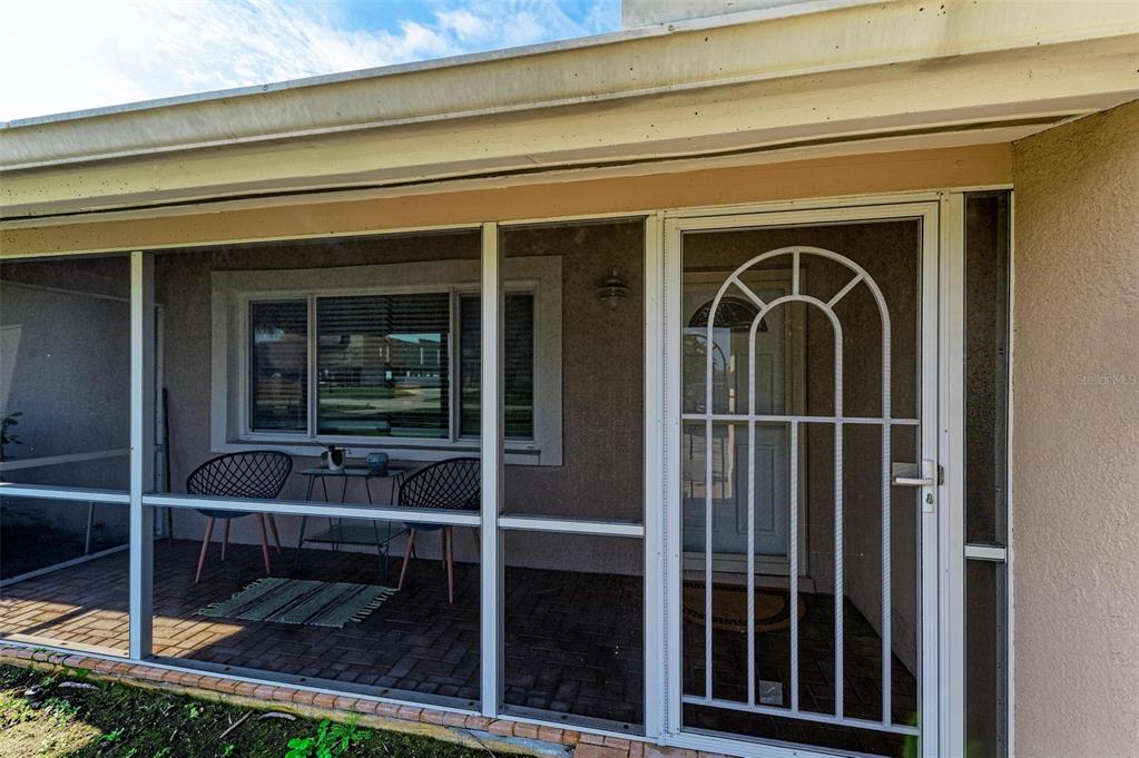 A screened-in porch features a brick floor, two chairs, a small table, and a screen door — 6000 BAYOU GRANDE BOULEVARD NE, ST PETERSBURG, FL