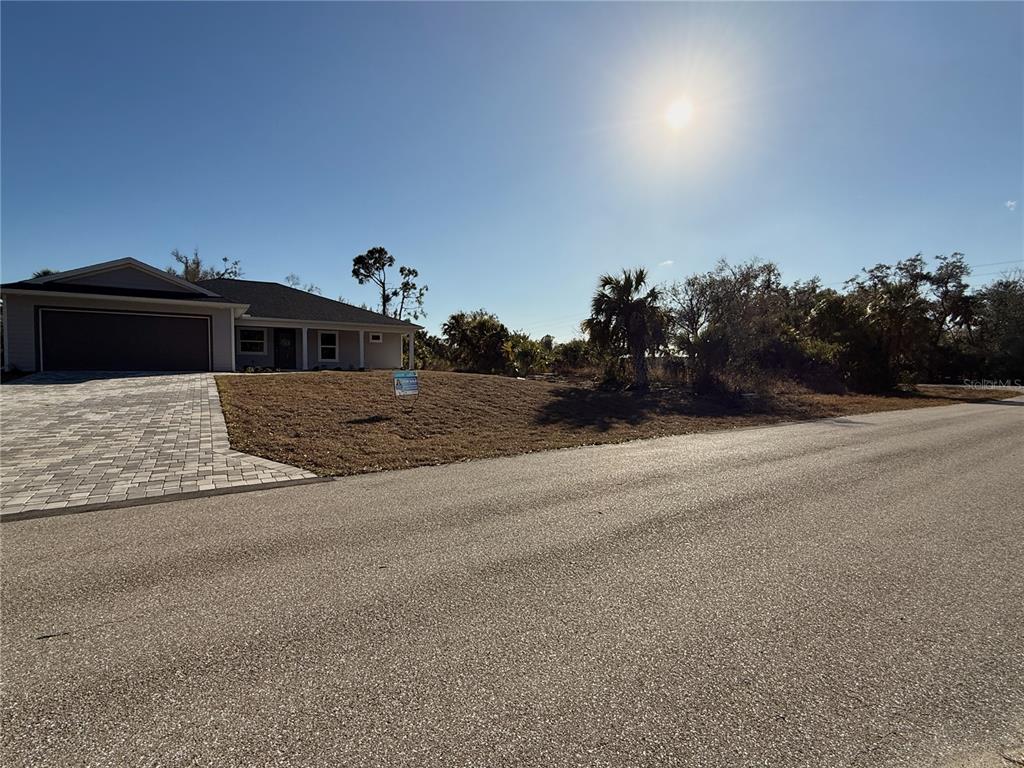 A single-story house with a paved driveway sits on a corner lot under a sunny sky — 16411 STRAUSS AVENUE, PORT CHARLOTTE, FL