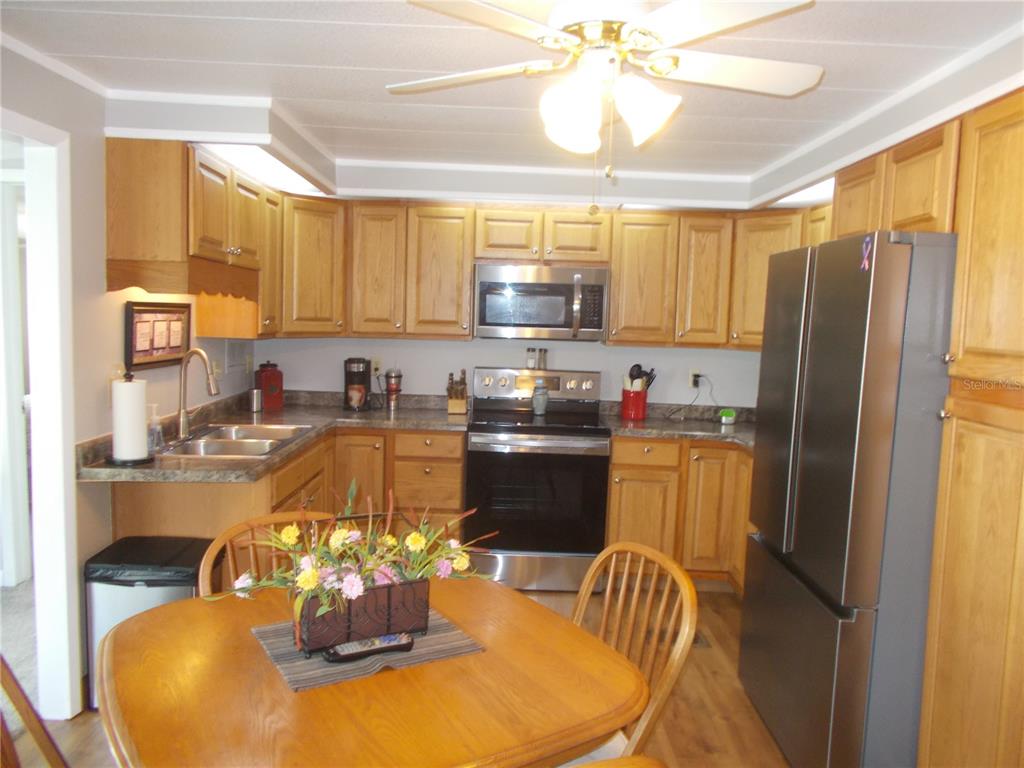 A kitchen with oak cabinets, stainless steel appliances, and a wooden dining table in the foreground — 5755 HOLIDAY PARK BOULEVARD, NORTH PORT, FL