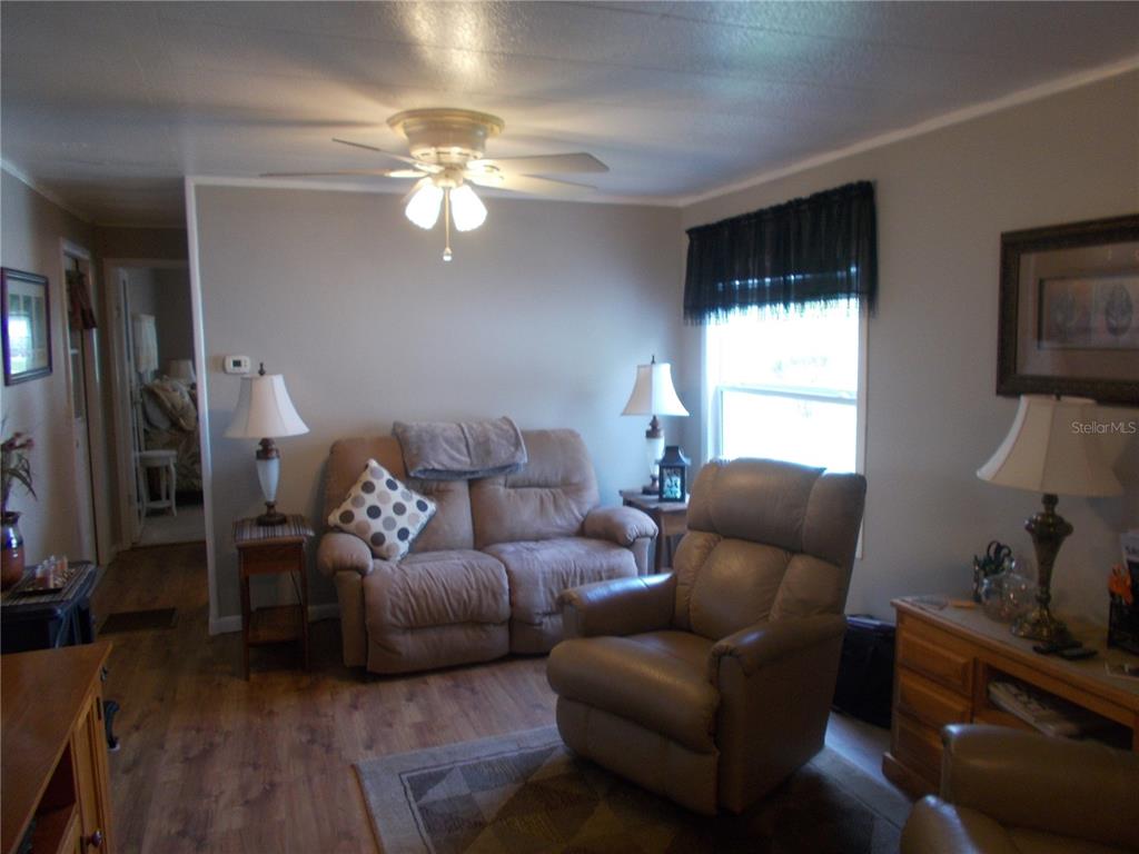 A living room features a loveseat, a recliner, wood-look flooring, and a ceiling fan — 5755 HOLIDAY PARK BOULEVARD, NORTH PORT, FL