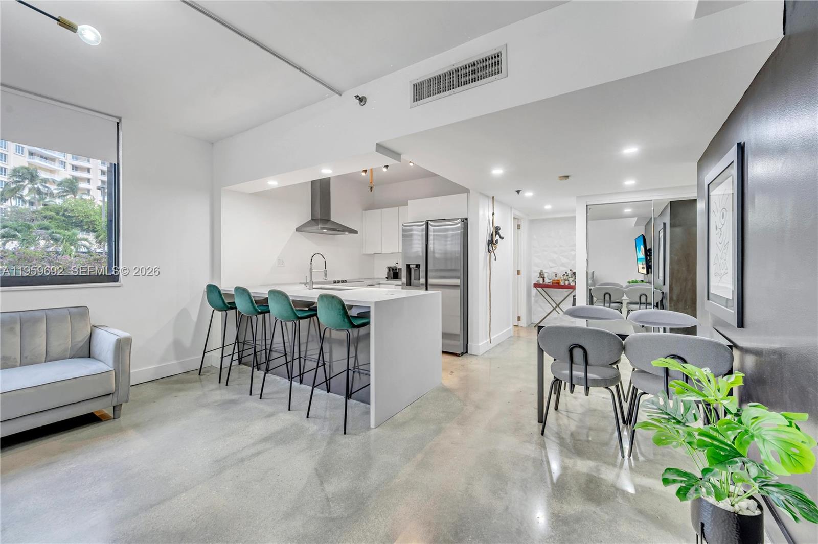 A modern open-concept kitchen and dining area features concrete floors, white cabinetry, and bar seating — 540 Brickell Key Dr # 409, Miami FL 33131, MIAMI, FL