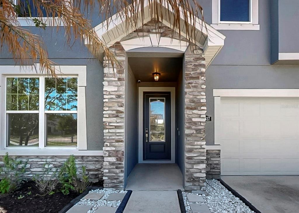 The exterior of a house features a stone-accented entryway, a dark front door, and garage — 12317 BAY ESTUARY BEND, RIVERVIEW, FL