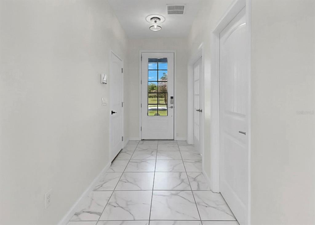 A bright entryway features white marble-look tile flooring, white walls, and a glass-paneled front door — 12317 BAY ESTUARY BEND, RIVERVIEW, FL