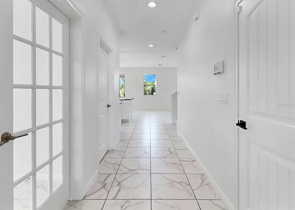 A hallway with white walls and marble-patterned tile flooring leads toward an open kitchen area — 12317 BAY ESTUARY BEND, RIVERVIEW, FL