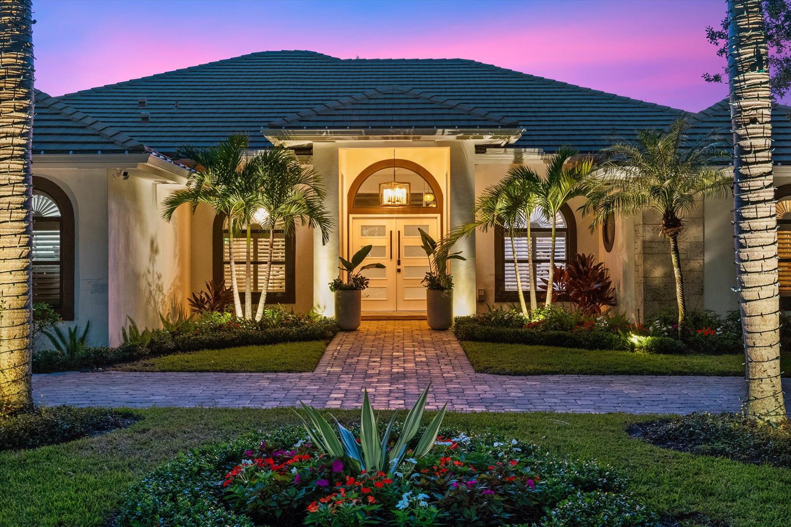 A single-story house exterior with a paved walkway, palm trees, and a lit front entrance — 18092 SE Laurel Leaf Lane, Jupiter FL 33469, JUPITER, FL