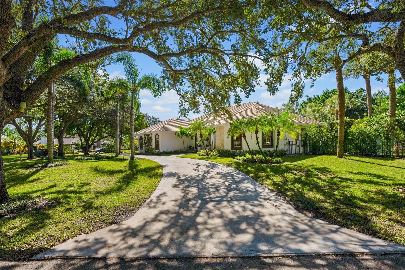 A single-story house with a concrete driveway, tile roof, and mature trees in the yard — 18092 SE Laurel Leaf Lane, Jupiter FL 33469, JUPITER, FL