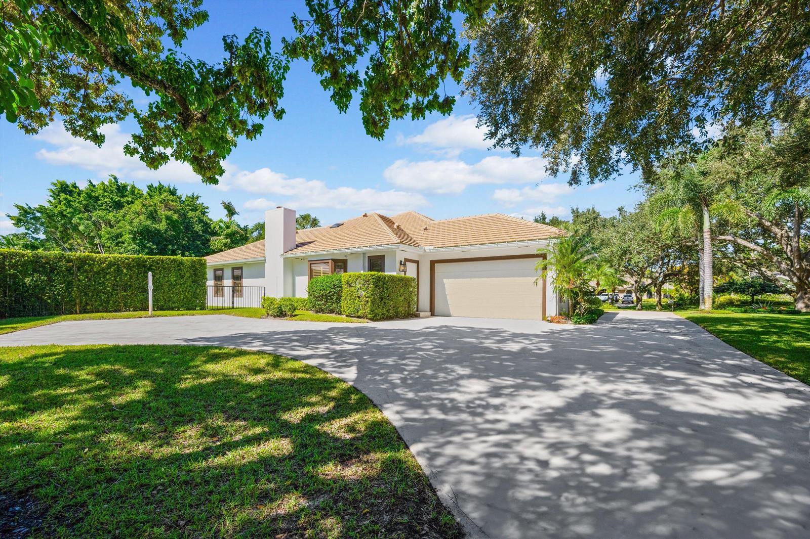 A single-story house with a tan tile roof, white exterior, and a large concrete driveway — 18092 SE Laurel Leaf Lane, Jupiter FL 33469, JUPITER, FL